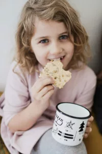 petite fille souriante qui mange une biscotte et qui tien une tasse en main